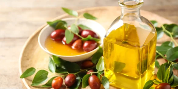 Jojoba oil bottle and jojoba fruits with leaves in a bowl, on a wooden tray.